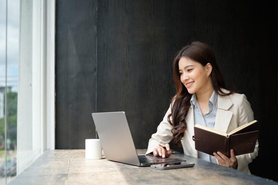 Profesional sonriendo frente a su laptop con una agenda en la mano